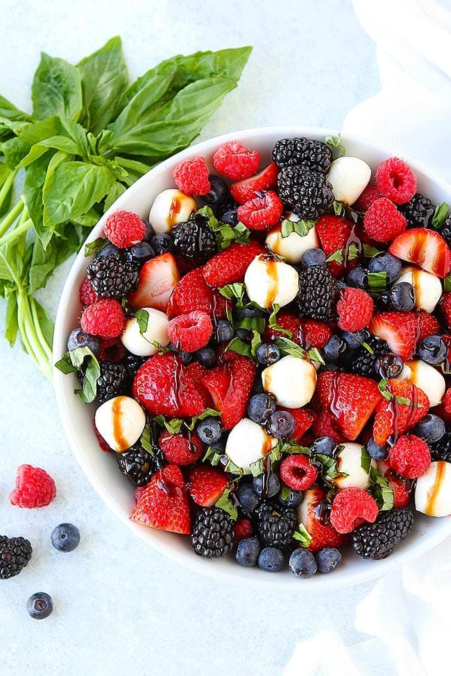This Beautiful Berry Caprese Salad Is A Great Simple Salad For Summertime! It Only Takes 10 Minutes To Make And Is The Perfect Side Dish To Go With Any Meal! #berry #berries #capresesalad #salad #cheese #mozarella #basil #balsamic #summer #vegetarian #glutenfree #easyrecipe #4thofJuly #redwhiteblue Berry Caprese Salad in bowl with basil.