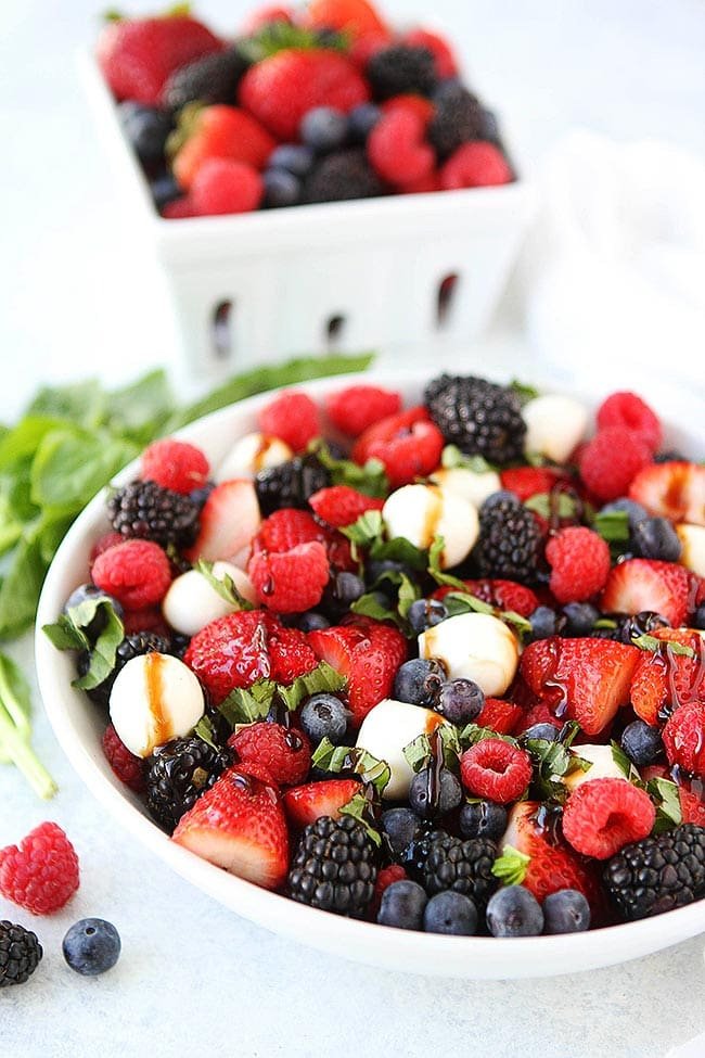 This Beautiful Berry Caprese Salad Is A Great Simple Salad For Summertime! It Only Takes 10 Minutes To Make And Is The Perfect Side Dish To Go With Any Meal! #berry #salad #summer #vegetarian #glutenfree #cheese #basil #easyrecipe #fruit #fruitsalad #easyrecipe #healthyrecipe #recipe Berry Caprese Salad with fresh mozzarella balls, balsamic glaze, and fresh basil in bowl.