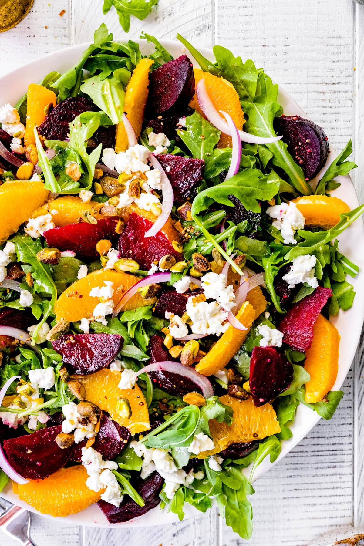 salad in bowl with arugula, beets, orange slices, red onion, pistachios, and goat cheese.