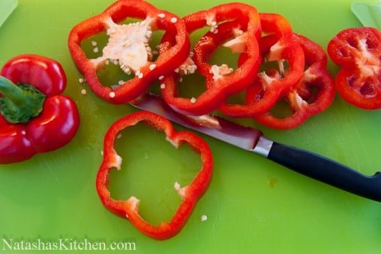 A red bell pepper being cut into rings on a cutting board 