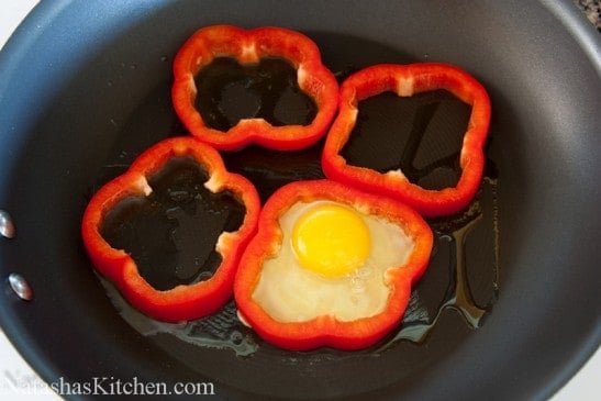 Four bell pepper rings on an oiled skillet and one pepper has an egg in it 