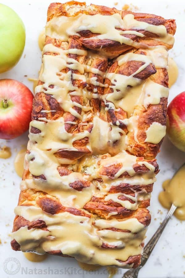 Apple bread loaf on a platter with a few fresh apples on the side.