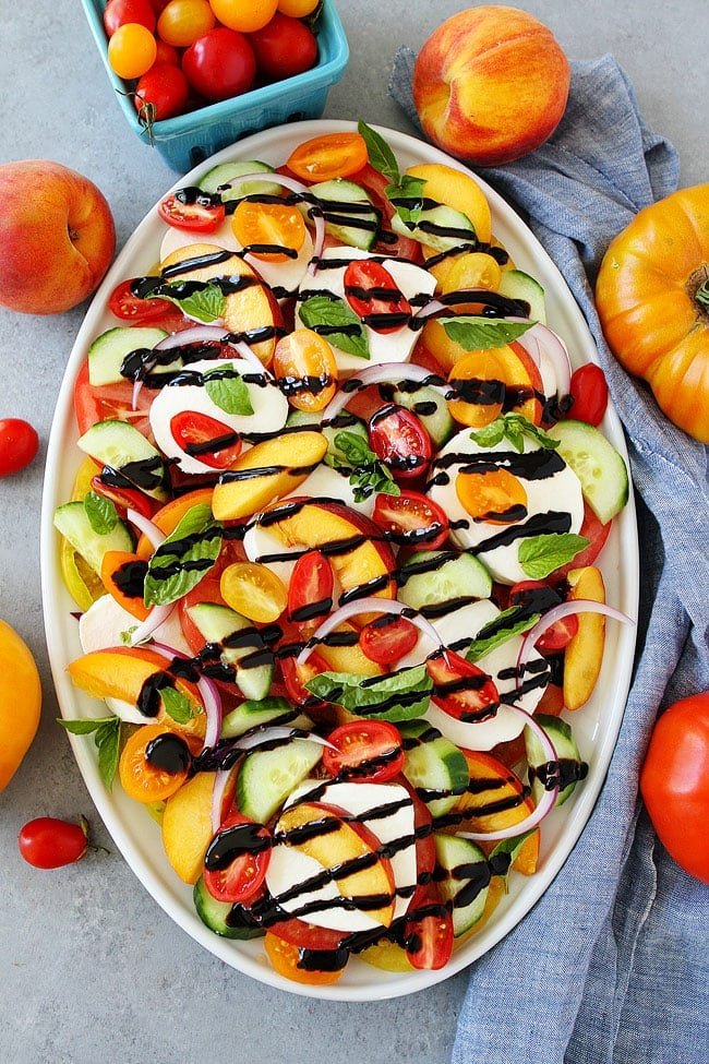 Summer Caprese Salad made with tomatoes, peaches, cucumber, fresh mozzarella cheese, red onion, basil, and a simple balsamic glaze.