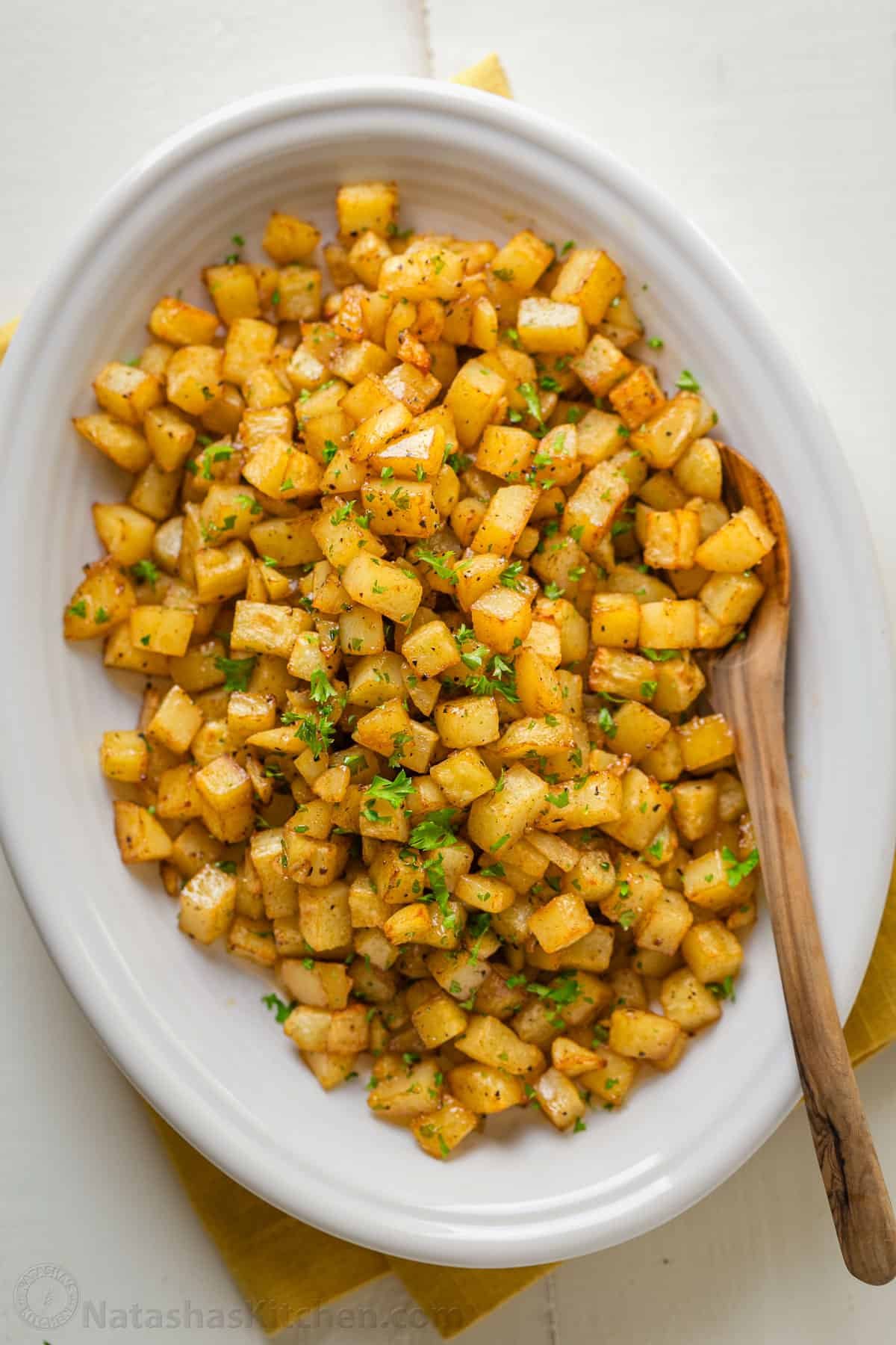 Our go-to, easy breakfast potatoes recipe uses simple ingredients and the best cooking method for potatoes, so each bite is delicious! easy Breakfast potatoes in a while serving dish with wooden spoon