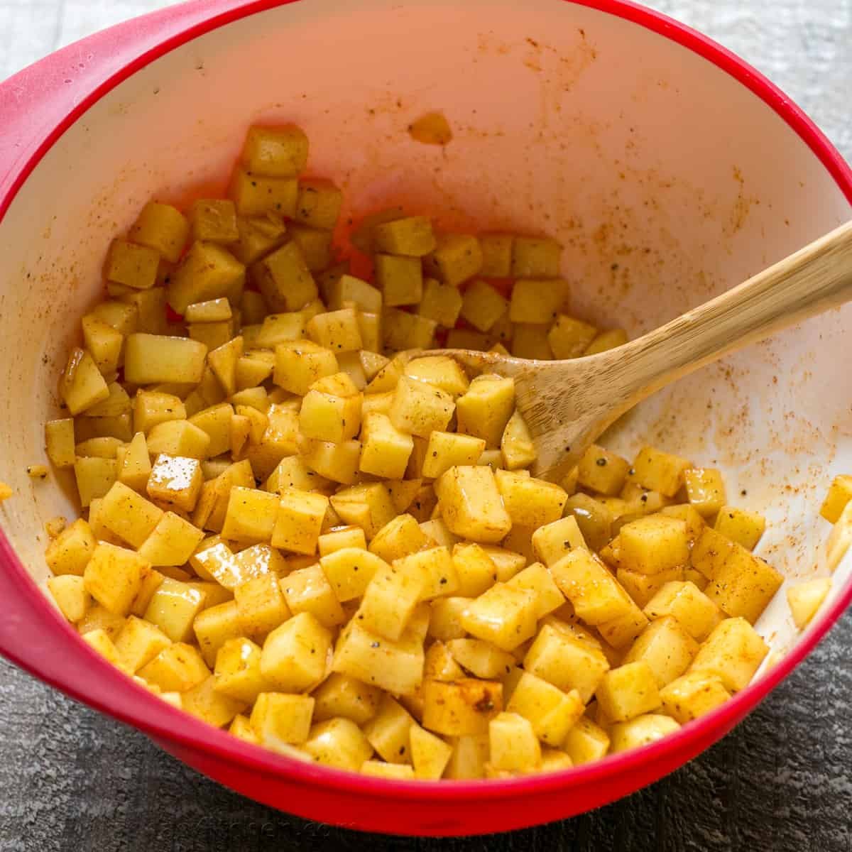 Our go-to, easy breakfast potatoes recipe uses simple ingredients and the best cooking method for potatoes, so each bite is delicious! cubed potatoes in a mixing bowl with spices and a wooden spoon