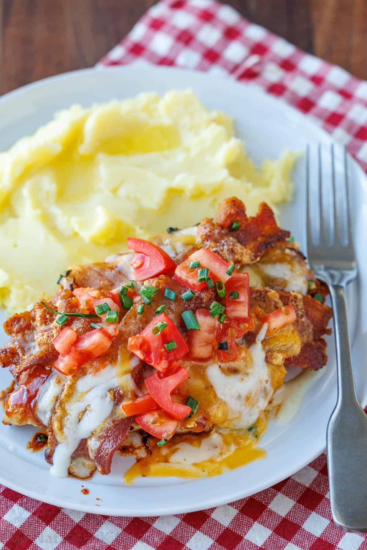Our Chili's copycat Monterey Chicken recipe brings the grilled chicken, tangy BBQ, smoky bacon, and gooey cheese restaurant favorite home to your kitchen. Monterey Chicken topped with melted Monterey jack cheese, tomatoes, crispy bacon, and chives. Served with mashed potatoes on a plate.