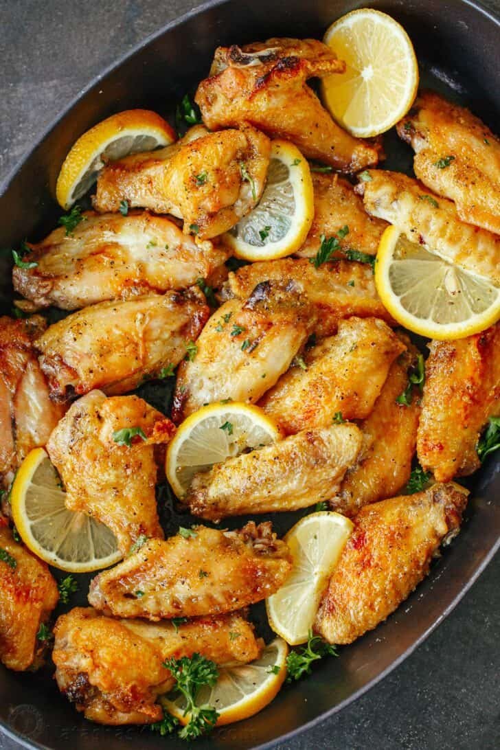 Baked Lemon Pepper Wings are crispy outside and tender inside. These chicken wings are coated in an irresistible lemon pepper butter sauce. Lemon pepper wings in a serving tray with lemons.