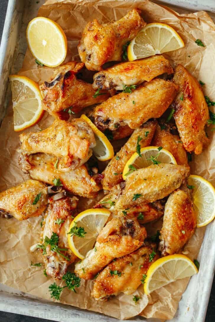 Baked Lemon Pepper Wings are crispy outside and tender inside. These chicken wings are coated in an irresistible lemon pepper butter sauce. Lemon Pepper wings baked on baking sheet and garnished with lemons