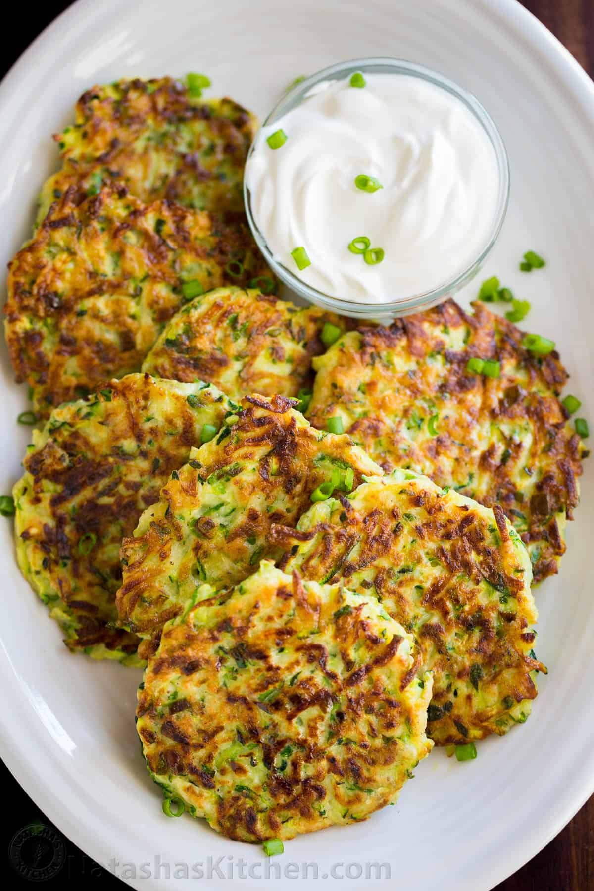 These crispy homemade zucchini fritters are a kid-friendly family favorite. An easy summer zucchini recipe you'll make again and again. Zucchini fritters on platter with cup of sour cream