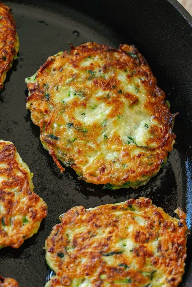 These crispy homemade zucchini fritters are a kid-friendly family favorite. An easy summer zucchini recipe you'll make again and again. Closeup of zucchini fritters in skillet