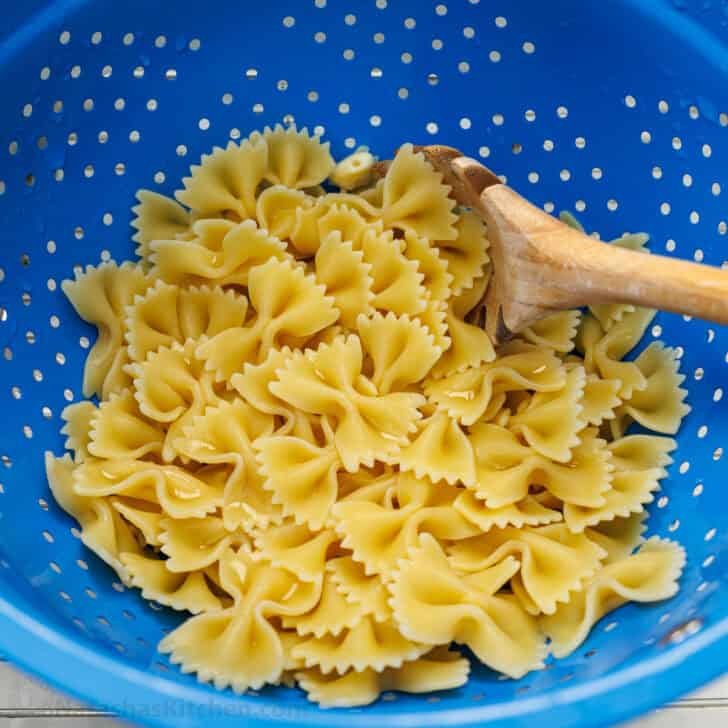 Greek Pasta Salad is a fresh, flavorful, and satisfying dish that brings a burst of Mediterranean flavor to any table. Perfect for any occasion and sure to please. Bowtie pasta, being cooked al dente and strained in a colander for Greek Pasta Salad