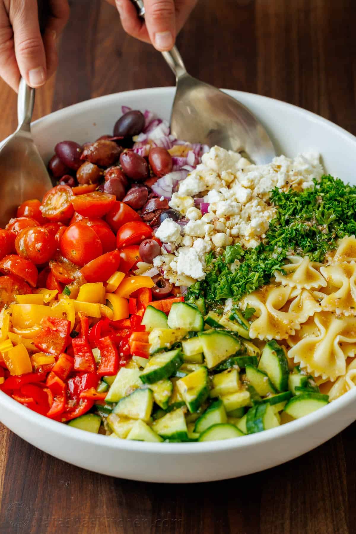 Greek Pasta Salad is a fresh, flavorful, and satisfying dish that brings a burst of Mediterranean flavor to any table. Perfect for any occasion and sure to please. Greek Pasta Salad ingredients being tossed in a white serving dish