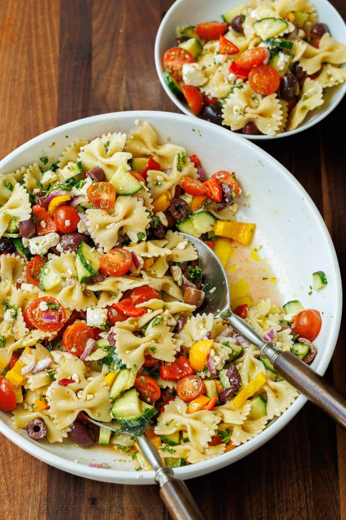 Greek Pasta Salad is a fresh, flavorful, and satisfying dish that brings a burst of Mediterranean flavor to any table. Perfect for any occasion and sure to please. Greek Pasta Salad tossed in a serving bowl with a serving spoon and a side portion in a smaller bowl on the side