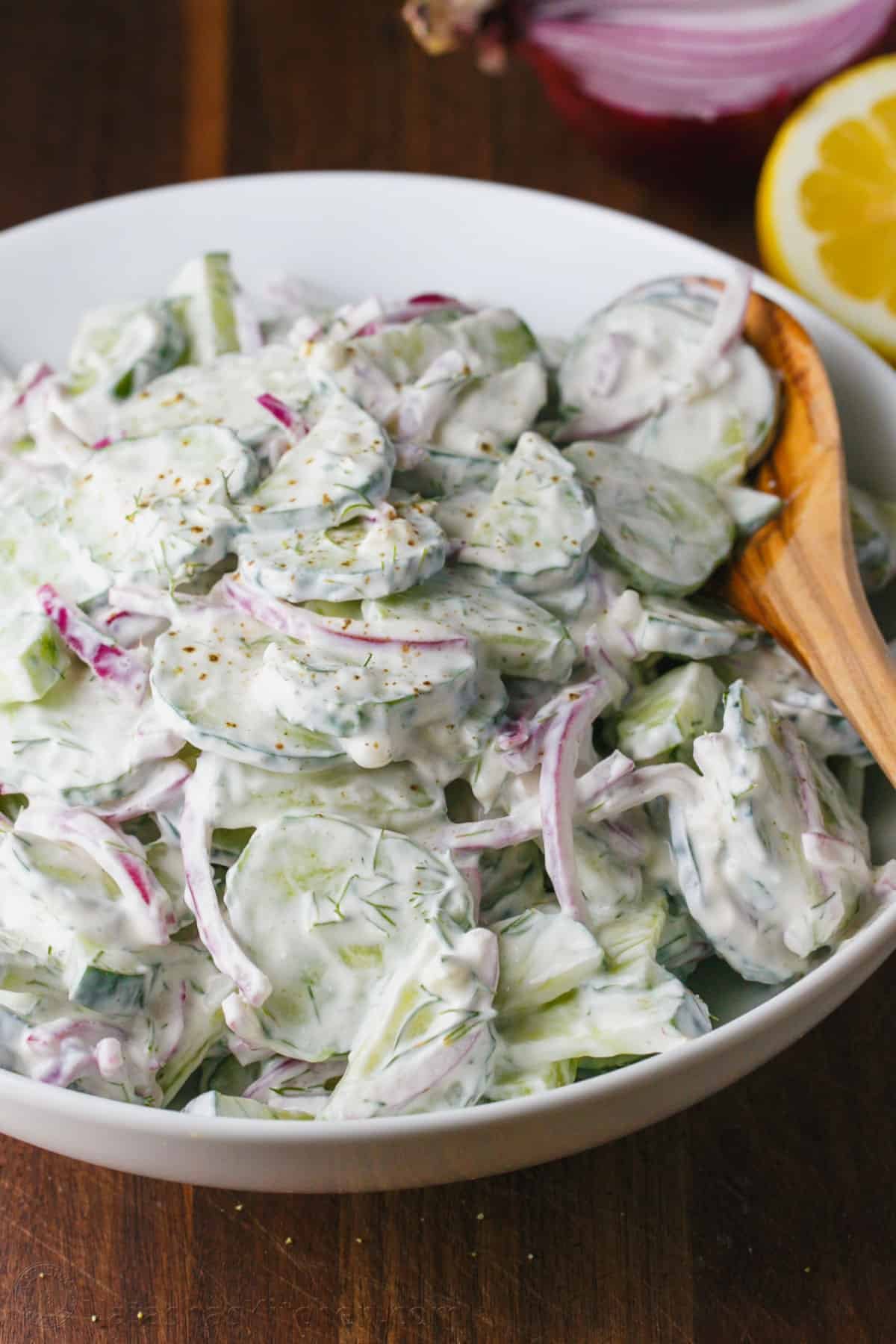 This easy Creamy Cucumber Salad combines cucumbers and red onions with a sour cream, lemon, and dill sauce that won't be able to resist! Bowl of creamy cucumber salad with serving spoon
