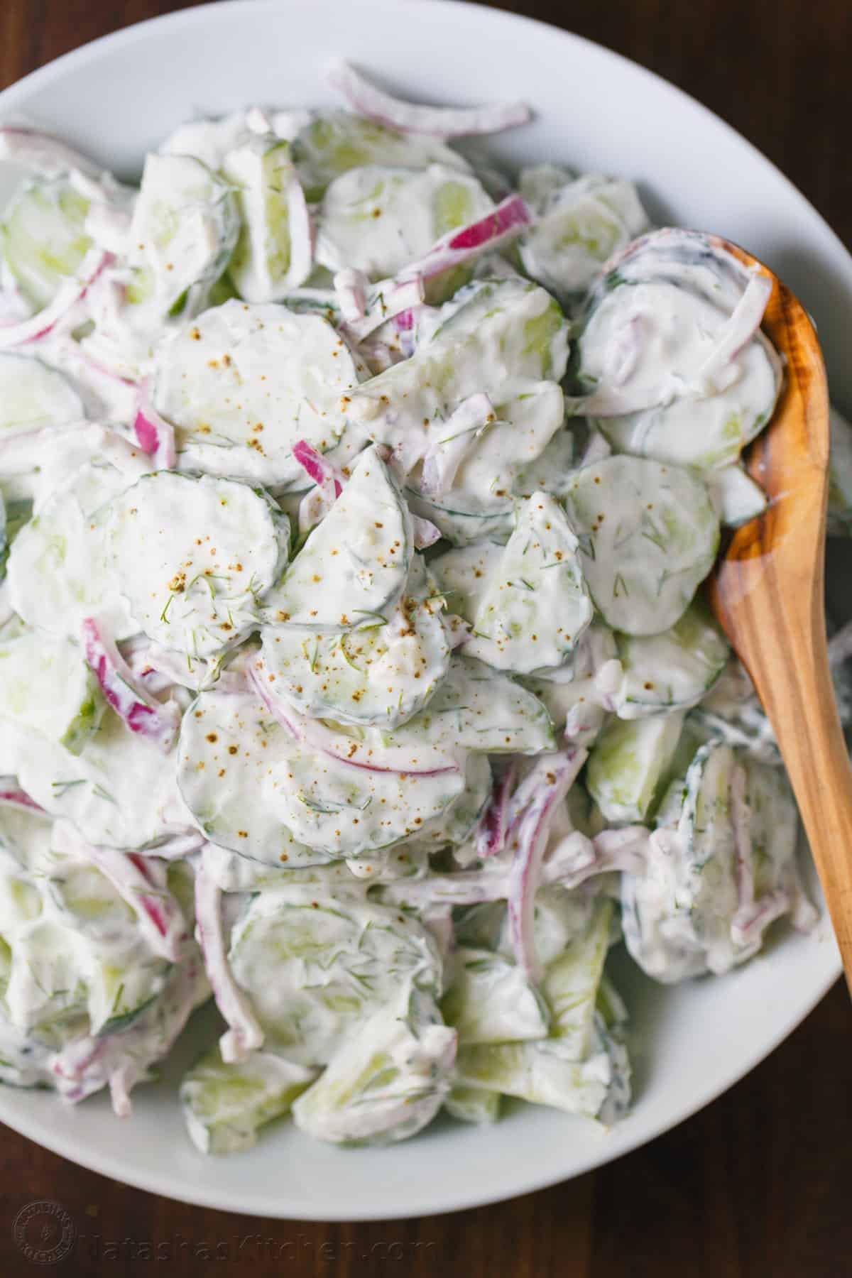 This easy Creamy Cucumber Salad combines cucumbers and red onions with a sour cream, lemon, and dill sauce that won't be able to resist! Creamy Cucumber Salad served in a bowl with a wooden spoon
