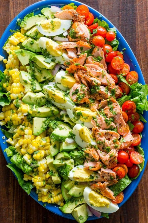 What is a cobb salad with layers of salmon, avocado, hard boiled eggs, corn and cherry tomatoes over romaine lettuce
