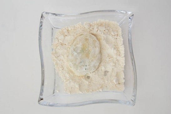 A parmesan and herb potato pancake being covered in flour in a bowl 