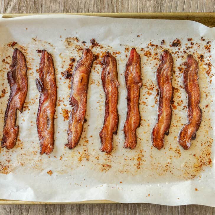 How to bake bacon in the oven that is perfectly crispy. Oven-baked bacon is the best for making a bigger batch and it's the easiest method. Oven-baked bacon slices on parchment paper