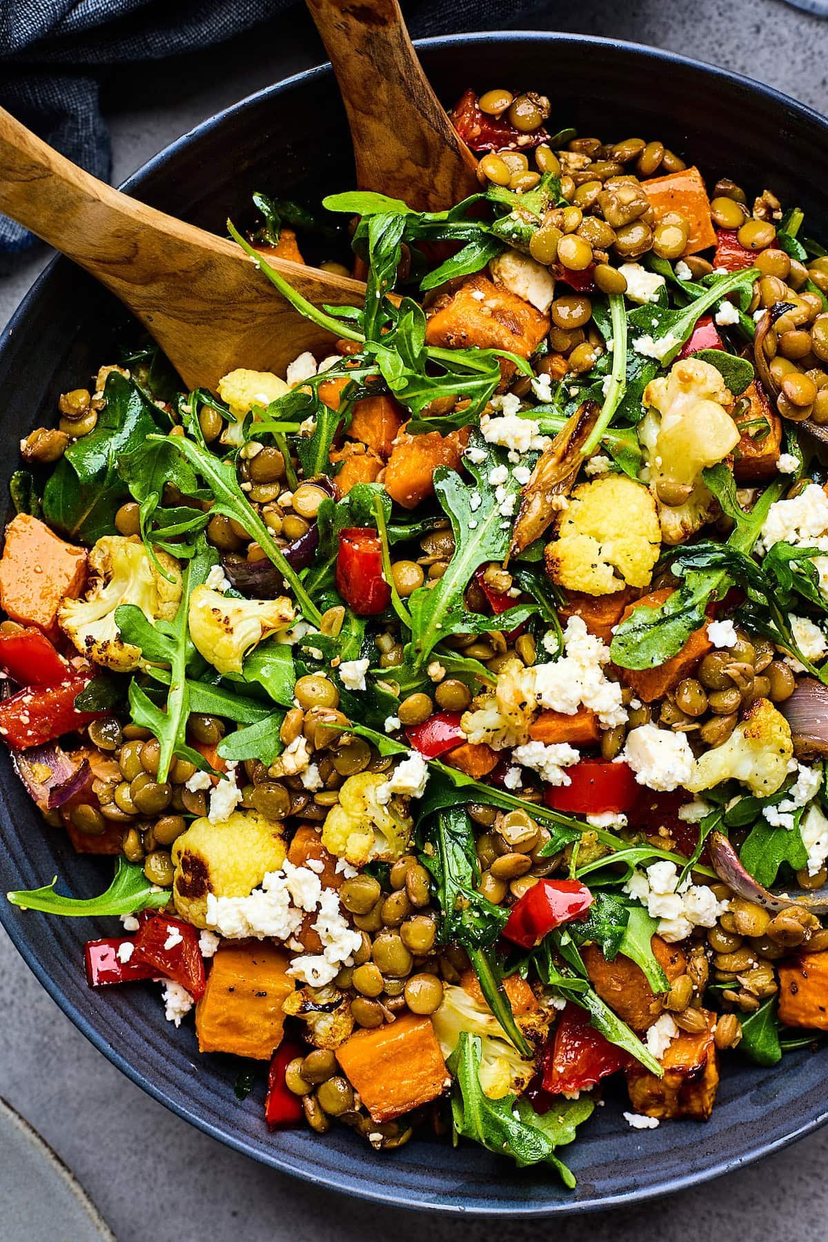 roasted vegetable lentil salad in bowl with wood salad servers.
