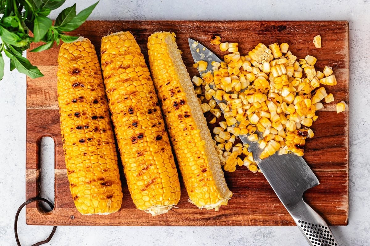 charred sweet corn on cutting board with knife.