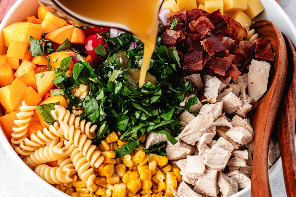 hot honey dressing being poured over chicken bacon peach pasta salad.