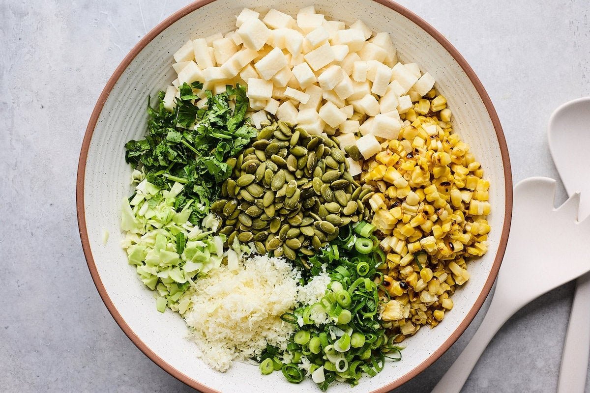 jicama, charred corn, green onion, cotija cheese, cabbage, cilantro, and pepitas in mixing bowl.