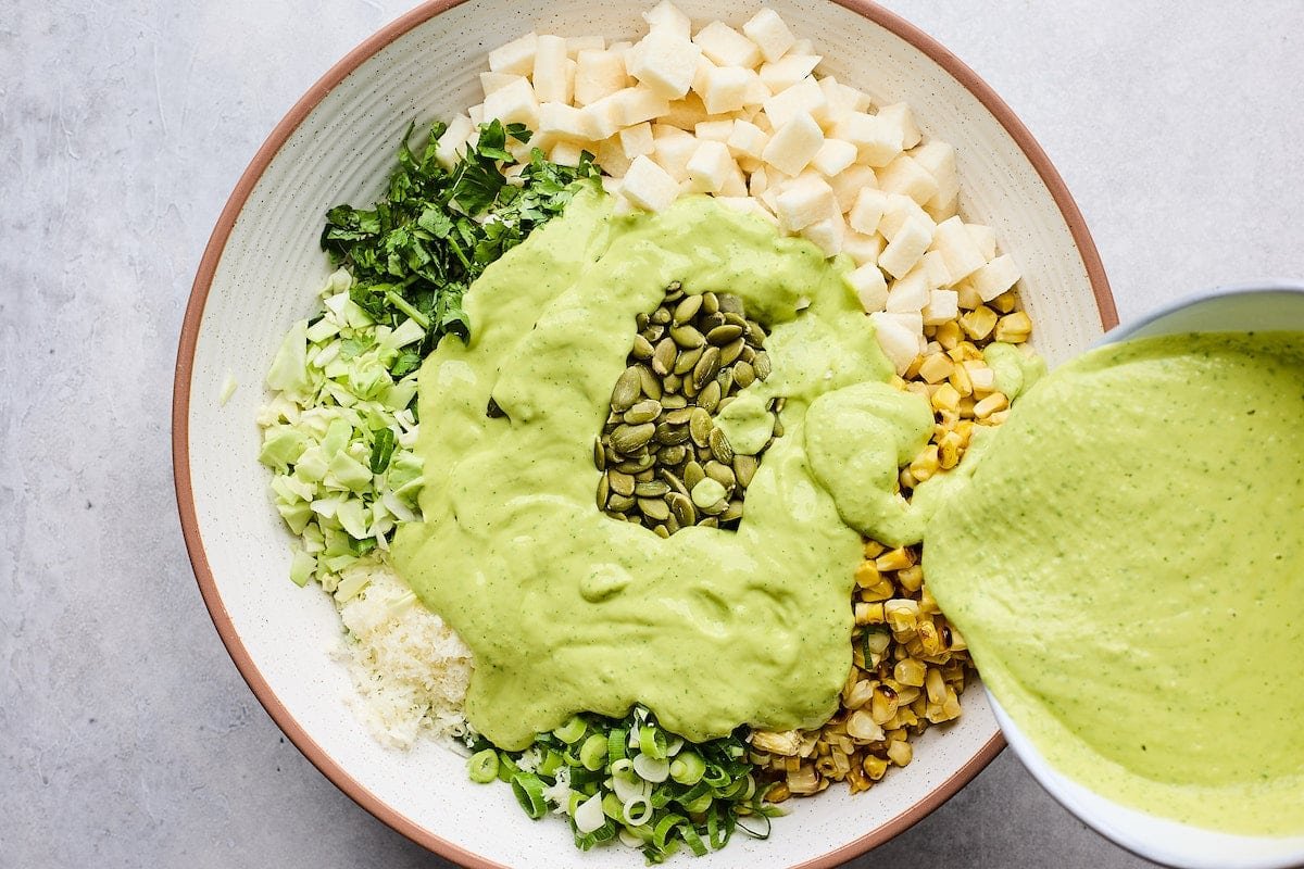 creamy avocado dressing being poured over charred corn cabbage salad.
