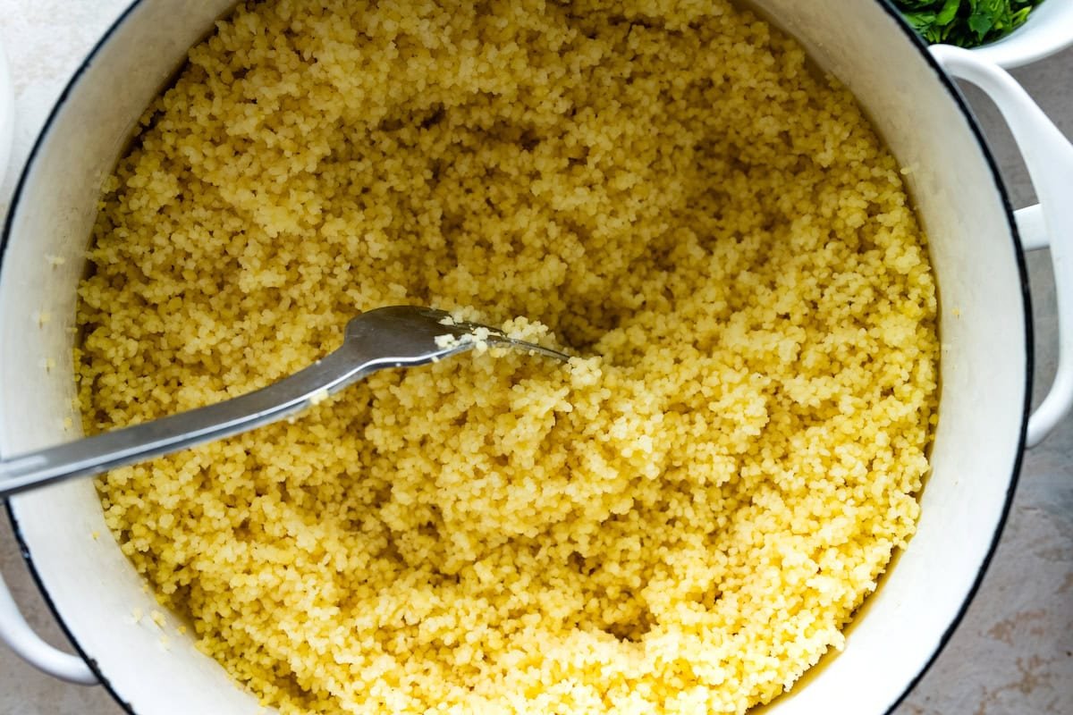 couscous being fluffed with a fork in big white pot.