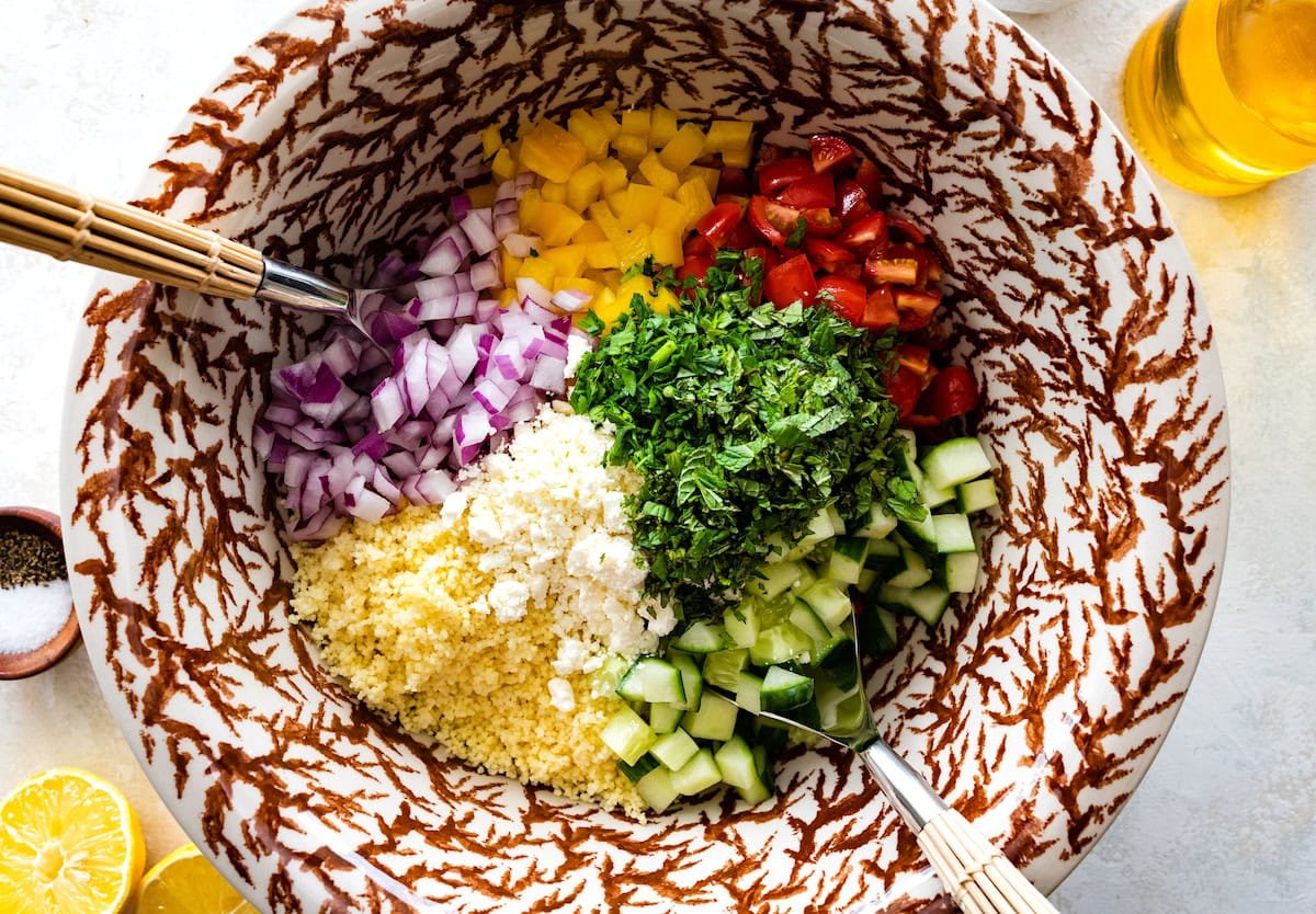 couscous, feta, cucumber, herbs, tomatoes, peppers, and red onion in mixing bowl to make couscous salad.