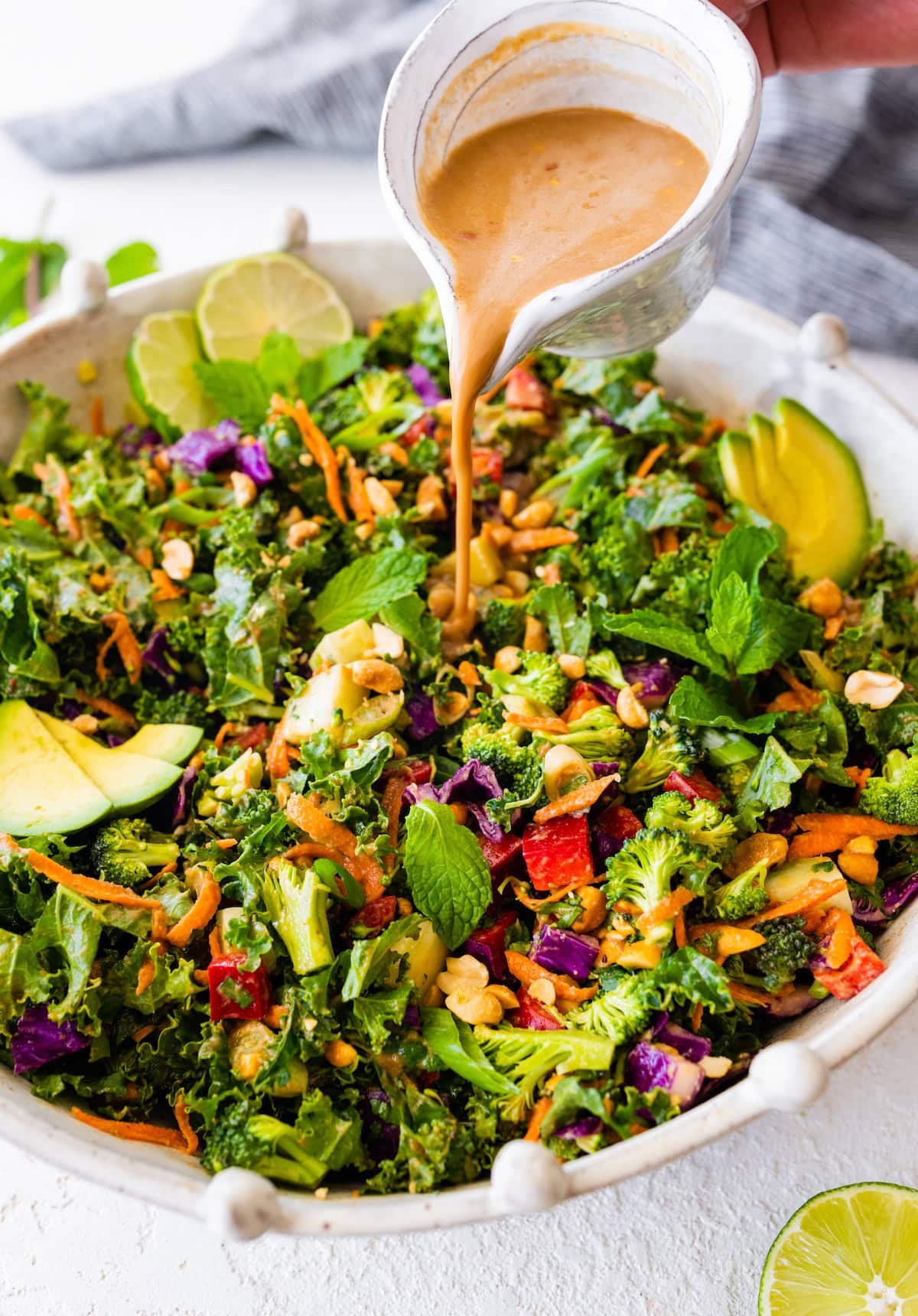 peanut dressing being poured over chopped kale broccoli salad.