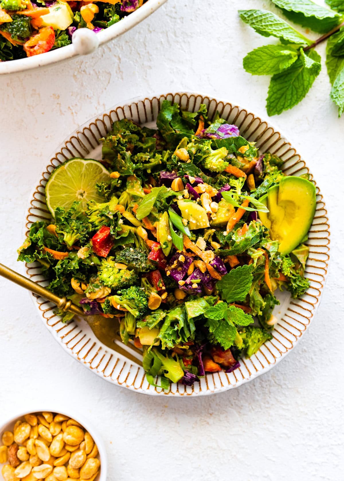 chopped kale broccoli salad with peanut dressing in bowl with lime, avocado, and a fork.