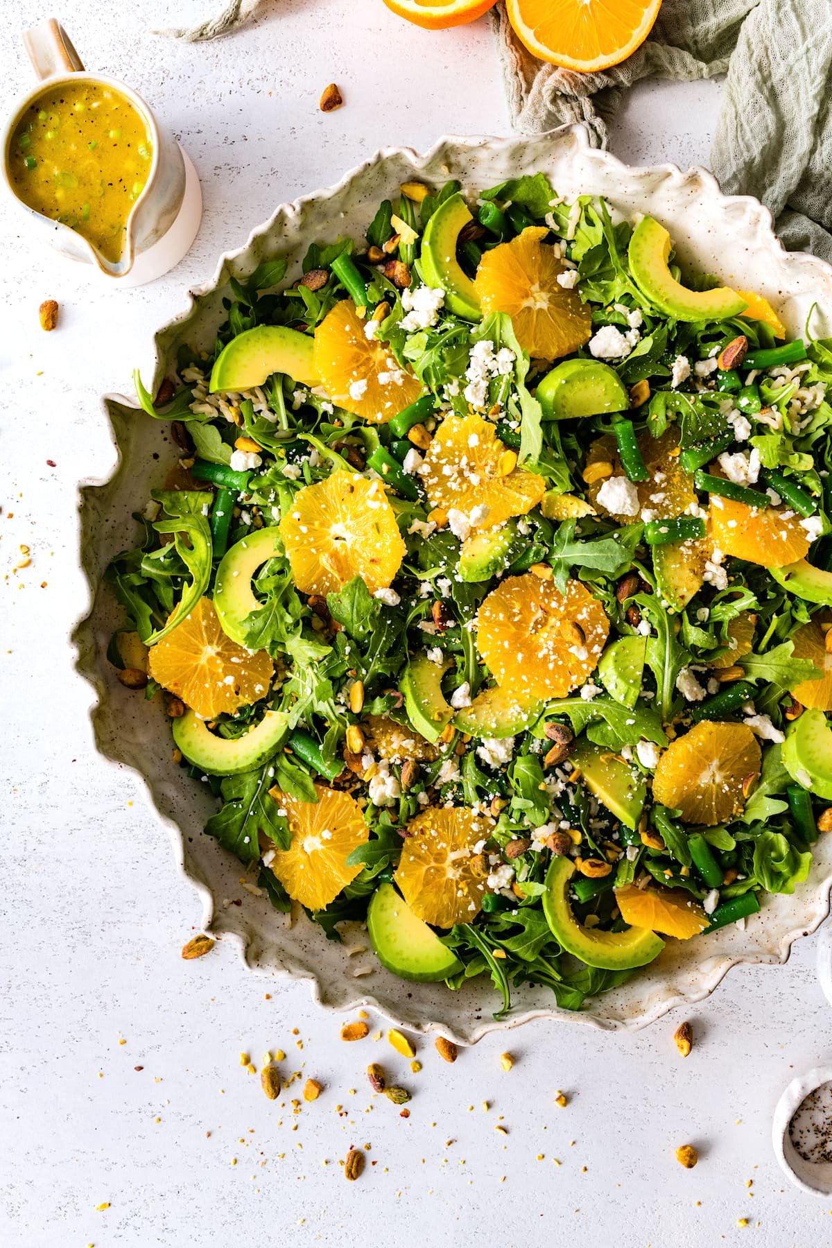 orange arugula salad in bowl with rice, green beans, feta, and pistachios.