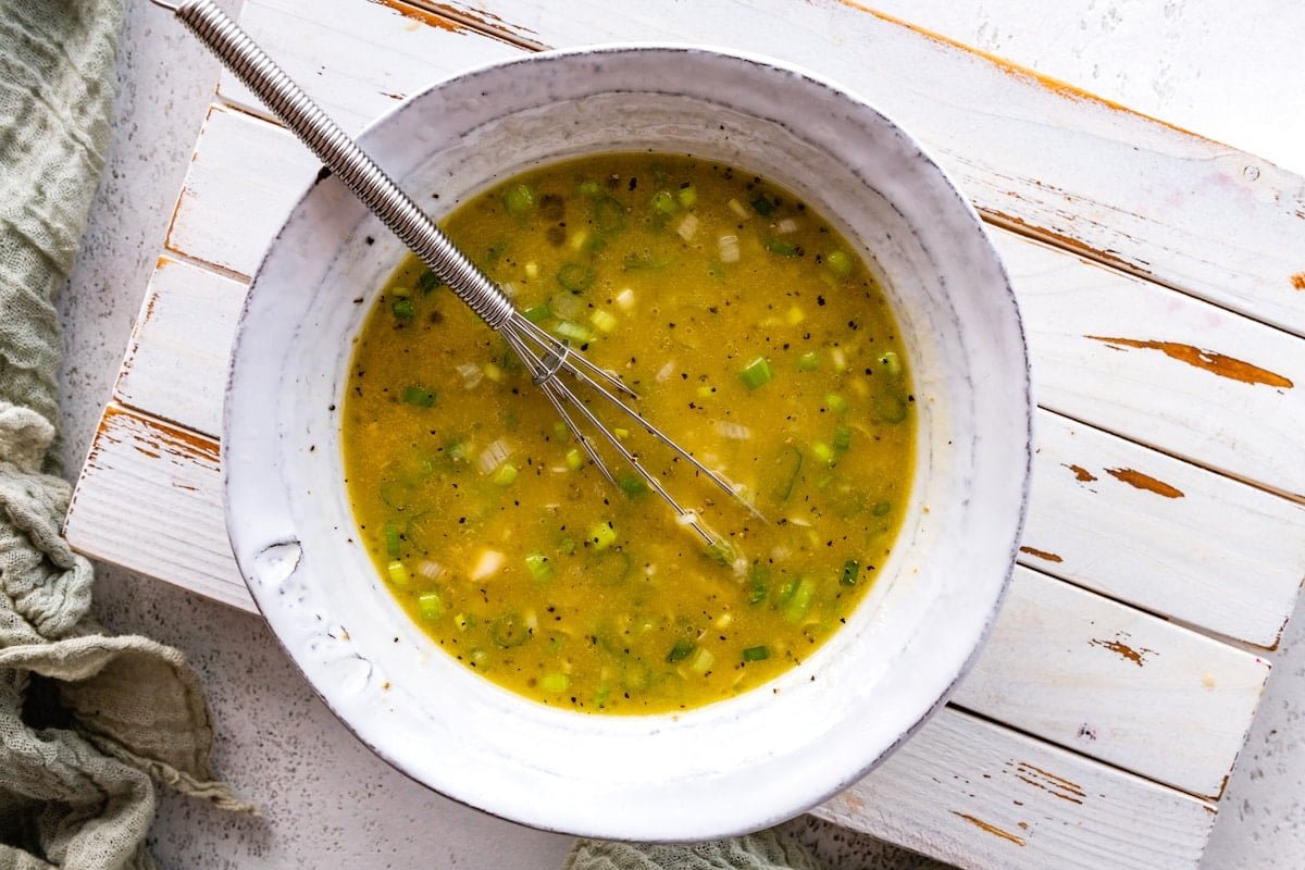 dressing in bowl with whisk to make orange arugula salad.