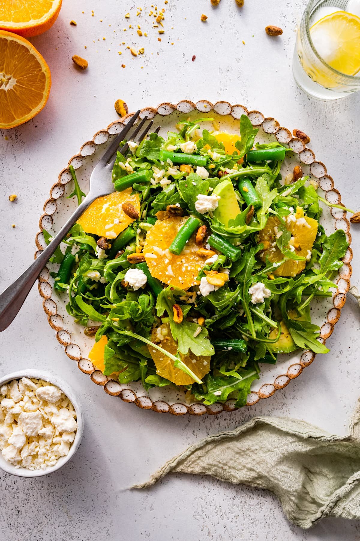 orange arugula salad on plate with green beans, rice, feta cheese, and pistachios.