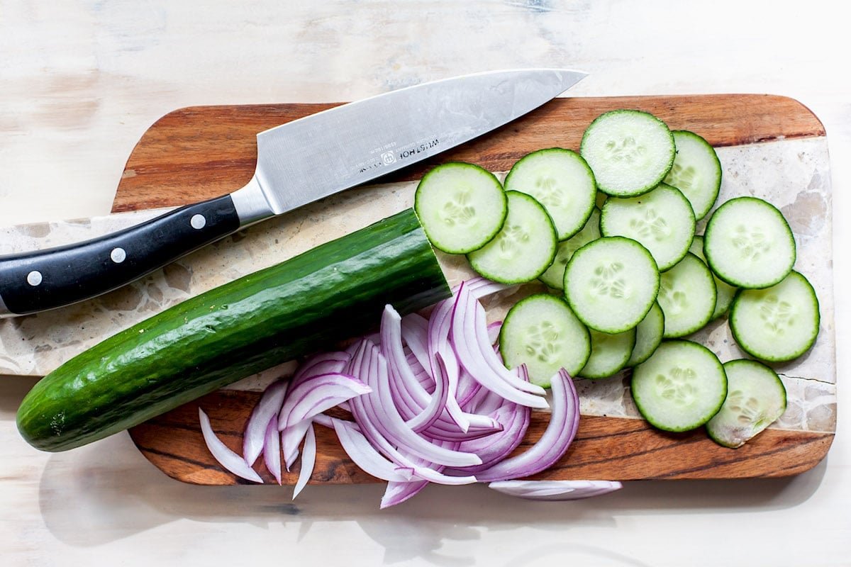 Cucumber and red onion on cutting board with knife.