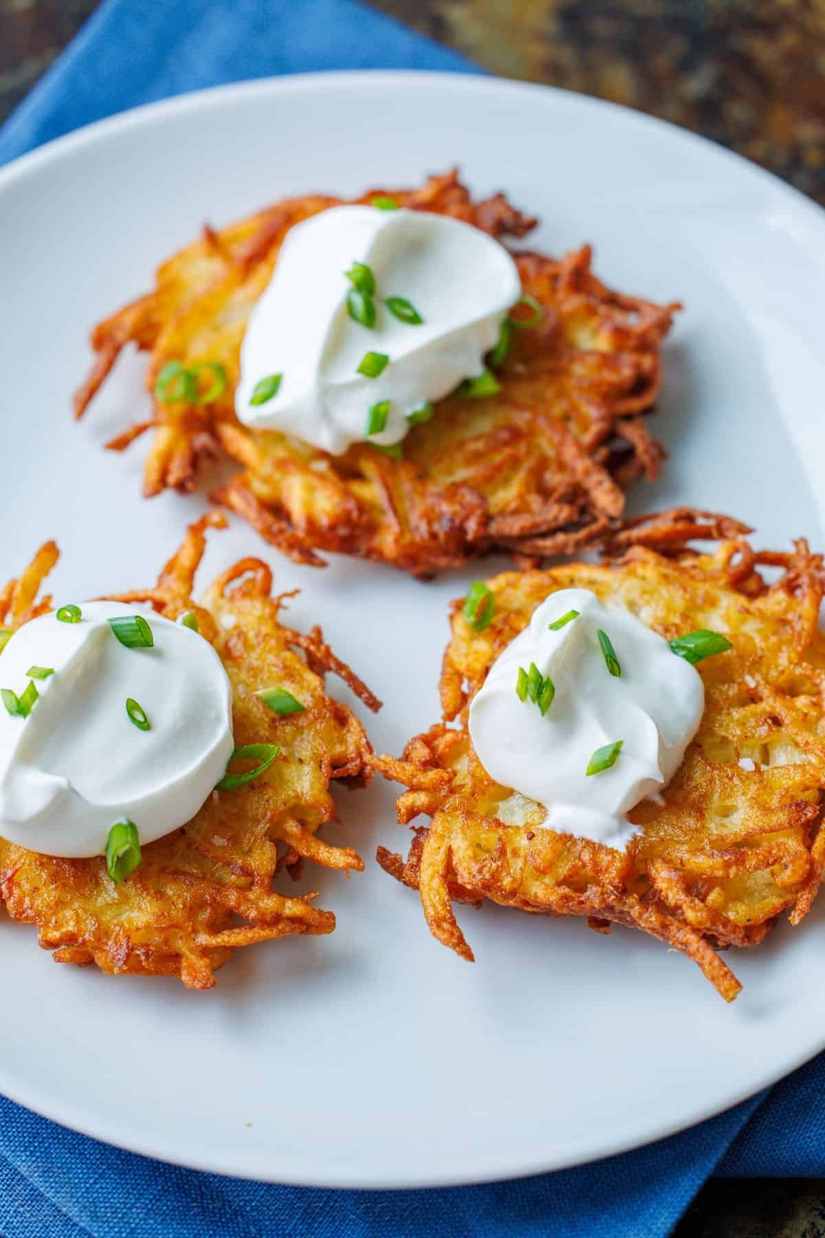 This latke recipe creates the crispiest potato fritters. Sprinkled with salt and dolloped with sour cream, these potato latkes are total comfort food. Latkes on plate with sour cream and chives