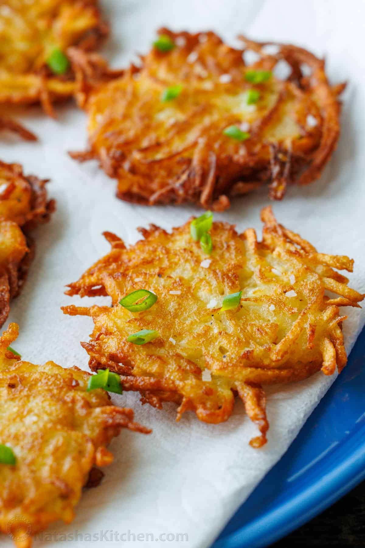 This latke recipe creates the crispiest potato fritters. Sprinkled with salt and dolloped with sour cream, these potato latkes are total comfort food. Latkes sprinkled with fresh chives on a plate