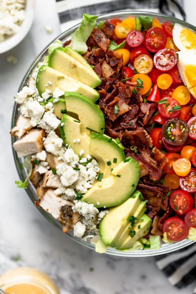 Cobb Salad With Chicken, Bacon, Tomatoes, Hard Boiled Eggs, Avocado, Blue Cheese, Chives, And A Simple Red Wine Vinegar Dressing. This Traditional Cobb Salad Is Loaded With Goodness And Always A Favorite! #salad #bacon #chicken #chickenrecipe #cobbsalad #avocado #eggs #glutenfree #glutenfreerecipe Easy Cobb Salad with chicken, bacon, avocado, cheese, tomatoes, and chives in large bowl.