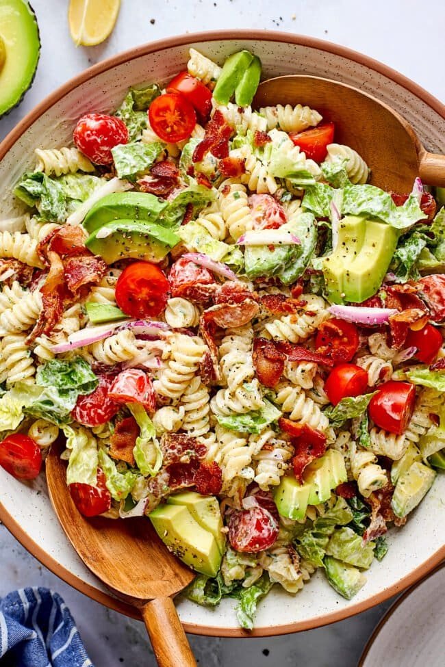 BLT pasta salad in bowl with wood serving spoons.
