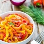 A bowl of zesty mini bell pepper salad with a fork, dill, mini peppers and purple onion beside it
