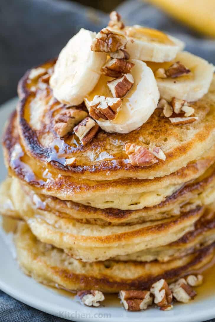 Stacked banana pancakes topped with bananas, pecans and maple syrup