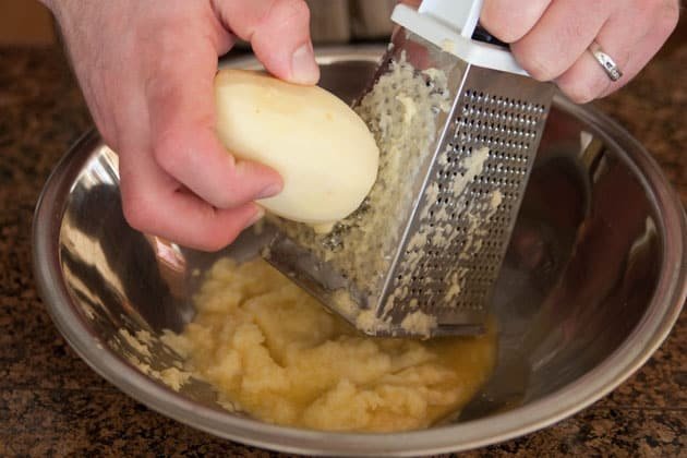 Potatoes being grated into a bowl 