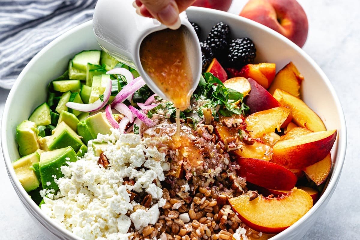 honey lime dressing being poured over blackberry peach arugula salad in bowl. 