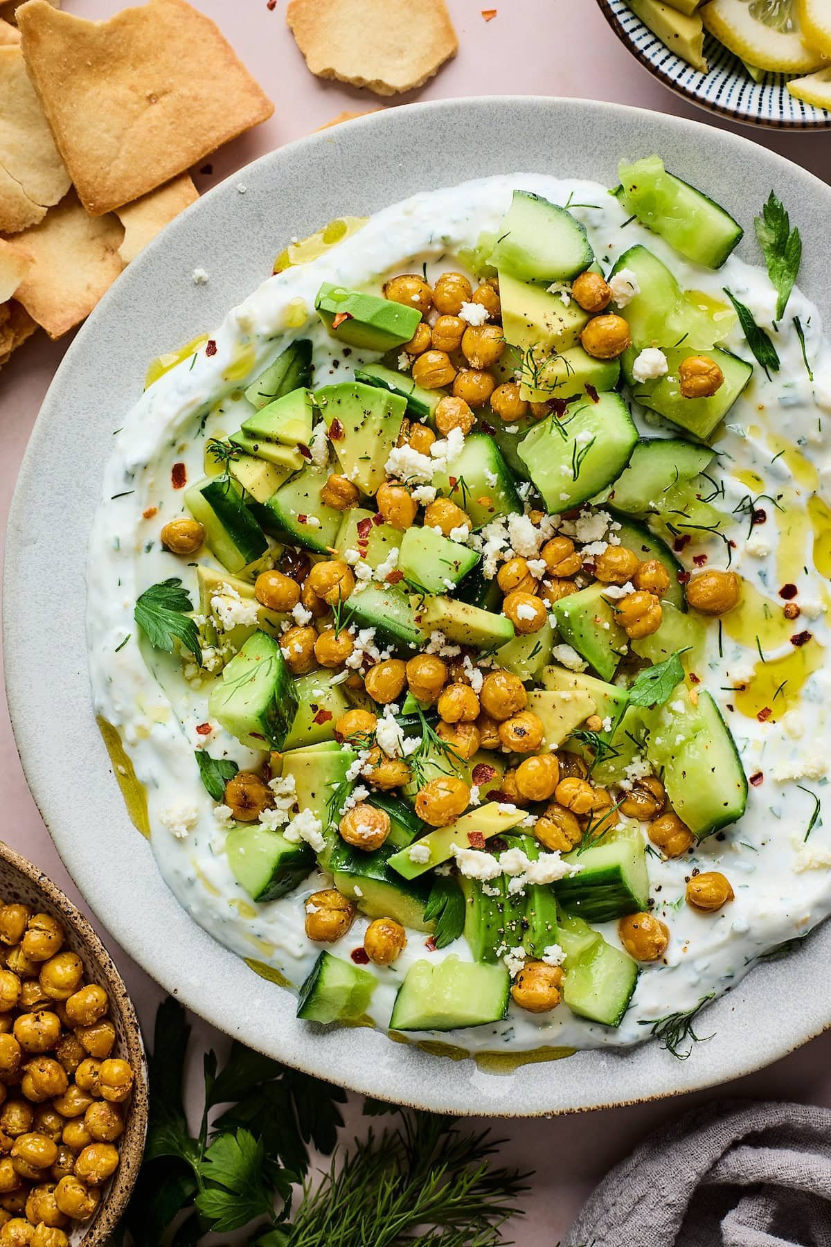 smashed cucumber, avocado, crispy chickpea salad with creamy yogurt feta spread on plate. 