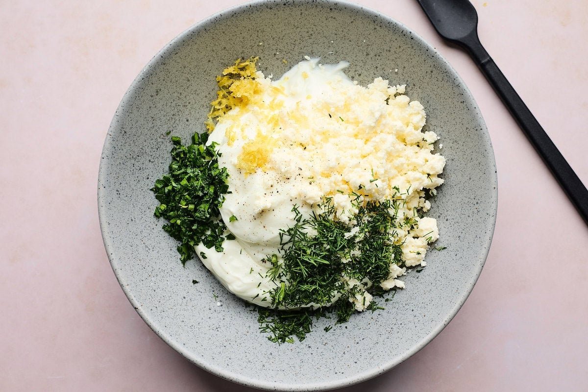 Greek yogurt, feta cheese, herbs, and lemon in bowl to make creamy yogurt feta spread. 