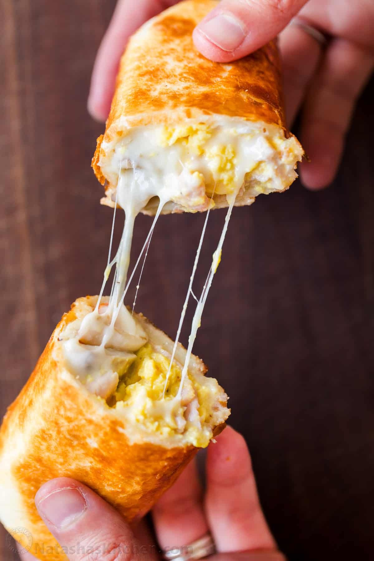 These Breakfast Burritos will make a breakfast person out of you. Crisp on the outside and filled with egg, ham, and cheese. Easy freezer breakfast burritos! Breakfast Burrito, sliced in half displaying scrambled eggs, ham, and stringy melted, mozzarella cheese