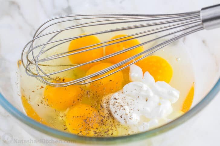 These Breakfast Burritos will make a breakfast person out of you. Crisp on the outside and filled with egg, ham, and cheese. Easy freezer breakfast burritos! Eggs and sour cream in a glass bowl with a whisk