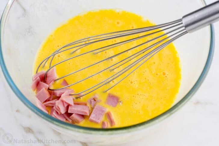 These Breakfast Burritos will make a breakfast person out of you. Crisp on the outside and filled with egg, ham, and cheese. Easy freezer breakfast burritos! Eggs and ham in a glass bowl with a whisk