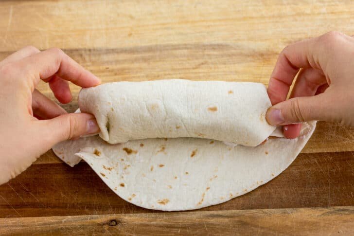 These Breakfast Burritos will make a breakfast person out of you. Crisp on the outside and filled with egg, ham, and cheese. Easy freezer breakfast burritos! Tuck the ends of the breakfast burrito in tightly