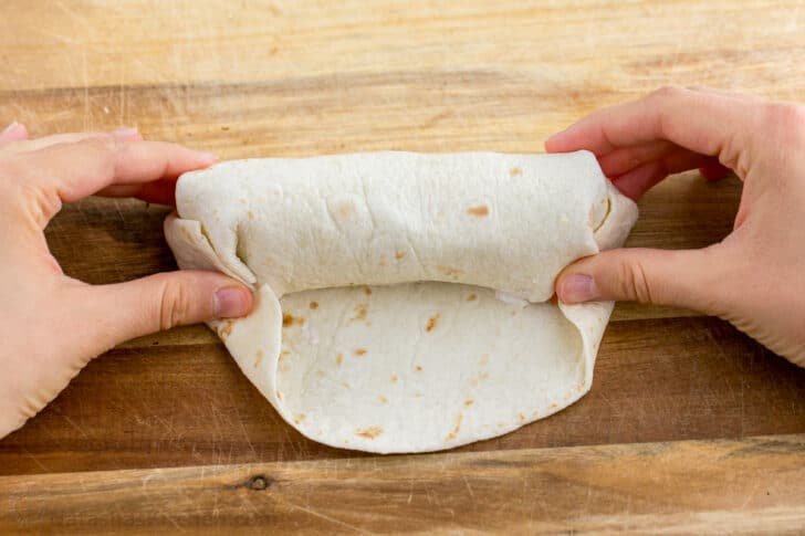 These Breakfast Burritos will make a breakfast person out of you. Crisp on the outside and filled with egg, ham, and cheese. Easy freezer breakfast burritos! Continue to pinch the ends of your tortilla as you wrap your breakfast burrito